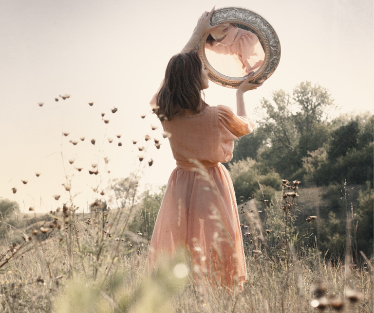 A woman in a field holding a mirror